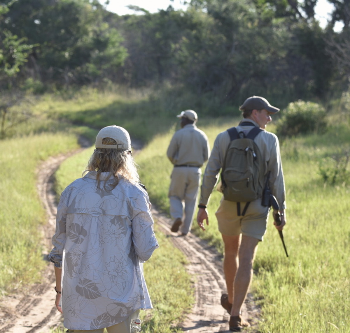 Two travelers walking a curving bush trail behind their private safari guide